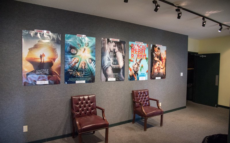 Five movie posters hang on a gray wall above two leather chairs in the Elbert Theatre lobby in Elberton, GA.
